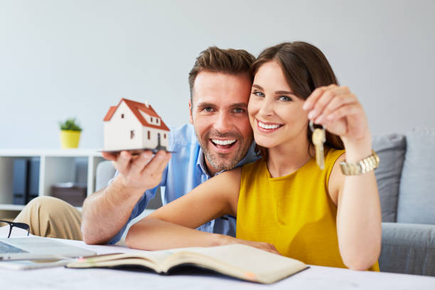 Happy couple holding keys to new home and house miniature - real estate concept